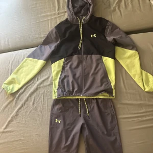 Grå och gul hoodie från Under Armour - Säljer en sportig grå och gul hoodie från Under Armour. Den har en dragkedja framtill och en justerbar huva. Perfekt för träning eller en avslappnad dag. Logotypen syns på bröstet och matchande byxor finns tillgängliga. Passar M mer tycker jag lite stor på mig fast den är S