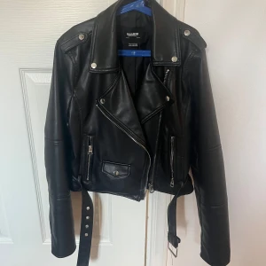 Svart skinnjacka från Pull&Bear - Snygg svart skinnjacka från Pull&Bear med dragkedja och bälte. Jackan har långa ärmar och flera dragkedjefickor framtill. I jätte bra skick därav att den är knappt använd. Står att den är strl M men hade sagt att den är mer än XS/S