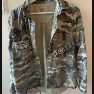Camouflage jacka - Snygg camouflage jacka med coola patches på. Perfekt för en avslappnad stil. Skjortan har långa ärmar och knappar framtill.