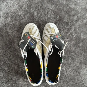 Vita fotbollsskor från Adidas - Snygga vita fotbollsskor från Adidas med svarta detaljer och snörning. Skorna har en unik design med mönstrade inslag och robusta dobbar för bra grepp på planen. Perfekta för fotbollsspelare som vill ha stil och funktionalitet. 2009 modell, ny pris 3000