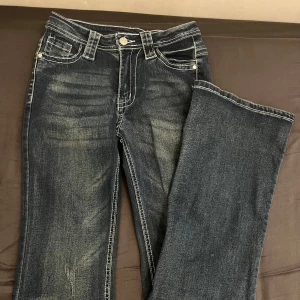Mörkblå jeans med kontrastsömmar - Snygga mörkblå jeans med vita kontrastsömmar och klassisk femficksdesign. Perfekta för en avslappnad stil med en touch av vintagekänsla.