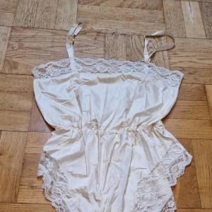 Spetsbody  - Cremefärgad spetsbody i satin med knäppning i grenen. Passar M. Justerbara axelband varav den ena lossnat lite där den ska gå ned vid skulderbladet. Skadar inte funktionen alls och lätt att åtgärda. Sparsamt använd. Katt i hemmet. 