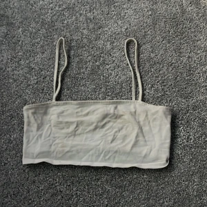 Vit tubtopp - Säljer en stilren beige tubtopp med smala axelband. Perfekt för varma dagar eller som ett basplagg i garderoben. Enkel och bekväm design.