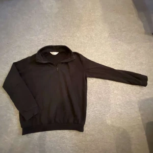 Svart tröja med dragkedja - Säljer en svart tröja med dragkedja vid halsen. Tröjan har långa ärmar och ribbade muddar vid ärmslut och nederkant. Perfekt för kyliga dagar.