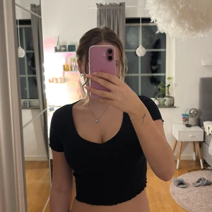 Svart croppad topp - Säljer en stilren svart croppad topp med korta ärmar och en djup v-ringning. 