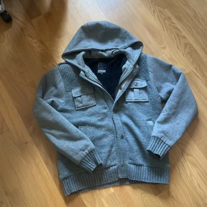 Grå cardigan från smog - Säljer en grå cardigan från Smog. Jackan har en mysig fleecefoder på insidan och ribbade muddar vid ärmslut och nederkant. Den har också praktiska fickor med knappar framtill och en dragkedja för stängning. Skriv vid minsta funderingar! Priset är inte satt i sten😁