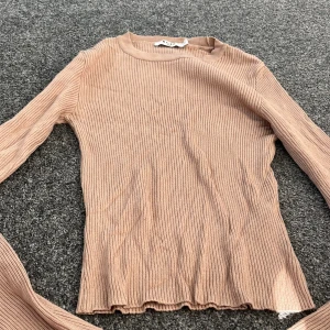 Beige ribbad tröja från NA-KD - Säljer en stilren beige ribbad tröja från NA-KD. Tröjan har långa ärmar och en enkel design som passar perfekt till olika outfits. Tillverkad i Turkiet och i storlek M. Perfekt för en avslappnad och trendig look.