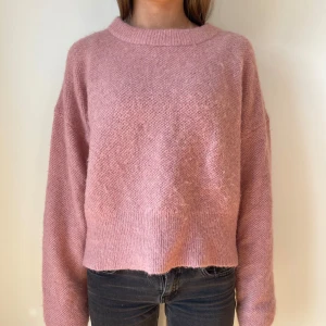 Rosa stickad tröja - Mysig rosa stickad tröja med en avslappnad passform. Tröjan har långa ärmar och en rund halsringning. Perfekt för kyligare dagar och ger en skön och stilren look.