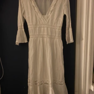 Vit klänning från H&M - Säljer en vacker vit klänning från H&M med spetsdetaljer och v-ringning. Klänningen har trekvartsärmar och en luftig passform, perfekt för sommarens alla tillfällen. Den är tillverkad i ett lätt och bekvämt material med ett inbyggt ”linne” för att den inte ska vara genomskinlig. Linnet går att klippa bort om man vill det. 
