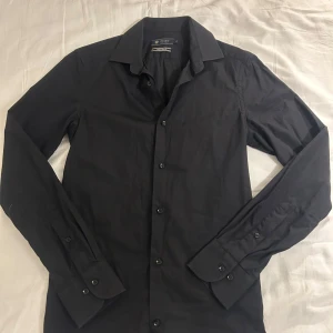 Svart skjorta från Riley - Snygg svart skjorta från Riley i super slim fit. Skjortan har långa ärmar och knappar framtill. Perfekt för en stilren look. Nypris 800
