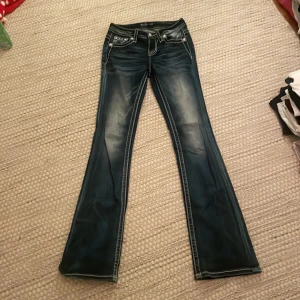 Blå jeans med broderad detalj - Snygga blå jeans med bootcut-stil och coola broderade detaljer på bakfickorna. De har en låg midja och framträdande sömmar som ger en unik look. Perfekta för dig som vill sticka ut!