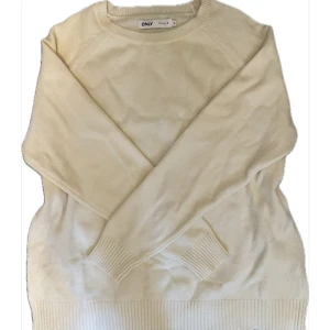 Gräddvit stickad tröja från ONLY - Enkel och stilren gräddvit stickad tröja från ONLY. Tröjan har rund halsringning, långa ärmar och breda ribbade muddar vid ärmslut och nederkant. Perfekt till allt i garderoben både till jeans och kjol. 