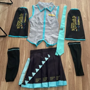 Vocaloid Miku cosplay kostym set - Miku cosplay kostym inspirerad av Vocaloid med grå väst med turkosa detaljer, svart plisserad kjol med turkos kant och gula mönster, matchande armvärmare och slips. Snygga grafiska tryck och futuristisk design. Perfekt för dig som älskar anime och japansk popkultur.