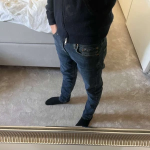 Replay Anbass jeans mörkblå herr - Säljer ett par snygga Replay Anbass jeans i mörkblå tvätt med klassiska femficksdetaljer och smal passform. Jeansen har orange kontrastsömmar och är tillverkade i mjukt denimtyg som sitter riktigt bra. Perfekta för dig som gillar stilrena och moderna jeans. Personen på bilden är 177! Köpta för 1499