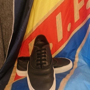 Saint laurent  - Svarta sneakers från Saint Laurent i grymt snyggt, kornigt skinn med vit platt sula. Klassisk låg modell med svarta snören och diskret branding på insidan och sulan. Perfekta för dig som gillar stilrena och lyxiga skor. Stl 42. Byten är väldigt intressanta vid möte. Kan mötas i täby, sthlm, Danderyd. Och andra områden vid överenskommelse 