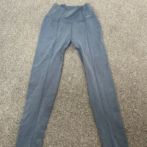 Blåa träningsbyxor från Aim’n med hög midja - Snygga blå leggings från Aim'n med hög midja och ribbade detaljer i midjan och benslut. De har dekorativa sömmar längs benen och är tillverkade i ett stretchigt material som sitter tight och bekvämt. Perfekta för en sportig och avslappnad look. Det ser ut som jeans material. Använda ungefär 2 gånger. Köpta för runt 650kr. 