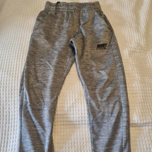 Nike Dri-Fit grå mjukisbyxor M - Grå Nike Dri-Fit mjukisbyxor med diskret mönster och svart Nike-logga på benet. Byxorna har elastisk midja med snörning. Slitage på knä, se bild. Därav priset. 