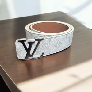 Vit bälte - Snyggt vitt bälte i skinn med klassiskt monogram och stor silverfärgad spänne. Bältet har en stilren design med diskreta mönster och passar perfekt till jeans eller kostymbyxor. Ett statement-accessoar för dig som gillar lyxiga detaljer.