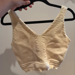 Stickad ljusbeige croppad linnetopp - Superfin stickad linnetopp i ljusbeige med breda axelband och ribbade detaljer. Toppen har v-ringning och snygga kabelstickade mönster längs banden och framtill. Aldrig använd