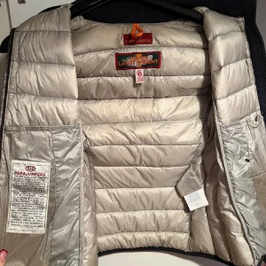 Svart dunväst från Parajumpers XS - Snygg svart dunväst från Parajumpers i storlek XS. Västen är quiltad med hög krage, dragkedja framtill och två fickor med dragkedja. Lätt och smidig att bära, perfekt för lager-på-lager-stil. Klassisk Parajumpers-logga bak i nacken. Finns en liten skavank och det är då att en av innerfickorna har lossnat och därav måste man sätta fast den med säkerhetsnål