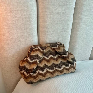 Zigzag clutch från Beck Söndergaard - Kuvertväska i bruna och beige toner från Beck Söndergaard. Väskan har ett snyggt zigzag-mönster, mjuk form och är tillverkad i ett stickat material. Invändigt finns ett fack med dragkedja och fodret är i matchande brun färg. Längd 31cm, höjd 20cm. Nypris 679kr så bra pris.