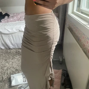 Beige långkjol med slits från Gina Tricot - Supersnygg beige långkjol från Gina Tricot i stretchigt material. Kjolen har rynkade detaljer längs sidan och en slits som ger en extra touch. Perfekt för dig som gillar en tight och figurnära passform.