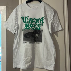 Vit Viagra Boys t-shirt med tryck - Vit t-shirt från Viagra Boys i storlek M med grönt grafiskt tryck och bild på en tax på framsidan. Klassisk passform med rund hals och korta ärmar. Materialet känns som bomull och baksidan har en liten svart illustration vid nacken. Aldrig använd 