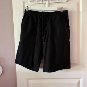 Svarta shorts med snörning - Svarta shorts med elastisk midja och snörning framtill. De har en enkel och clean look med rak passform och är perfekta för varma dagar. Materialet känns lätt och bekvämt, vilket gör dem grymma för chill eller aktivitet.