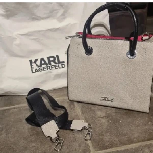 Karl Lagerfeld - Snygg handväska från Karl Lagerfeld med svarta handtag och detaljer. Väskan är i äkta skinn och har en avtagbar axelrem i svart och beige. Insidan har en cool röd kant och väskan stängs med dragkedja. Stilren väska i mycket bra skick.