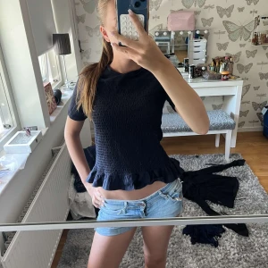 Svart smockad topp med volangkant - Supersöt svart topp med smockat tyg och volang längst ner. Kortärmad och figurnära passform som ger en trendig look. Perfekt att styla med jeans eller kjol för en chill vibe. 💕💕