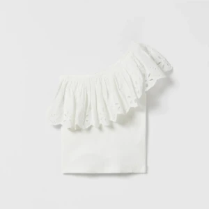 Vit offshoulder topp med volang - Superfin vit offshoulder topp med bred volangkant och broderade detaljer. Toppen är ärmlös och har en romantisk känsla med sin utskurna axel och spetsliknande brodyr. Perfekt för varma dagar och somriga outfits.