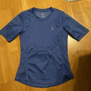 Blå tränings-tshirt från SOC - Sportig blå t-shirt från SOC med korta ärmar och rund hals. Tillverkad i ett lätt och snabbtorkande syntetmaterial som passar perfekt för träning. Snygga sömdetaljer och diskret logga på bröstet ger en clean look. Tror den är helt oanvänd. 