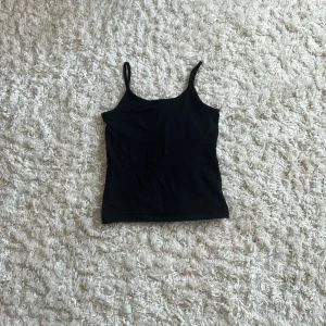 Svart linnetopp från H&M - Enkel svart linnetopp från H&M med smala axelband och rak passform. Perfekt att styla med jeans eller shorts för en clean look. Tillverkad i mjuk bomull som känns skön mot huden.