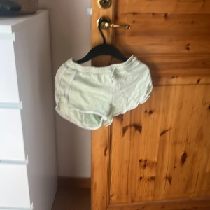 Mintgröna shorts från H&M - Snygga mintgröna shorts från H&M med vit broderad text på sidan. De har elastisk midja och vita detaljer längs kanterna. Perfekta för varma dagar eller chill hemma. Mjukt bomullsmaterial som känns skönt mot huden.