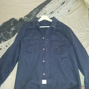 Blå overshirt från Gant i manchester - Säljer en snygg blå overshirt från Gant i manchestertyg. Skjortan har två bröstfickor med lock, klassisk krage och knäppning framtill. Perfekt lager-på-lager-plagg med avslappnad passform.