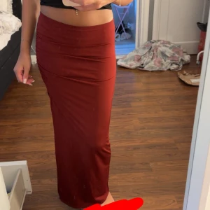 Mörkröd långkjol med slits - Säljer en snygg mörkröd långkjol med tight passform och slits på sidan. Kjolen har rynkade detaljer upptill och är i ett mjukt, stretchigt material som sitter skönt på kroppen. Perfekt för dig som vill ha en stilren men ändå trendig look.Storleken är Xs petite, så liten i storlek!