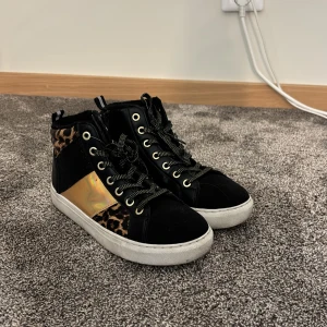 Svarta high top sneakers med leoparddetaljer - Coola svarta high top sneakers med leopardmönster och guldiga detaljer på sidorna. 