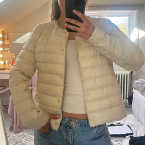 Beige pufferjacka utan krage från uniqlo - Säljer en beige pufferjacka med rund halsringning och knäppning framtill från uniqlo. Jackan är lätt vadderad och har inga större detaljer. Bilderna är från förra tjejen. Säljer igen då den inte kom till användning💗