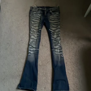 Blå slitna bootcut jeans low waist  - Säljer ett par blå jeans med kraftiga slitningar framtill, bootcut-modell och fransand midja. Jeansen har stora bakfickor med lock och knapp. Pris kan diskuteras 
