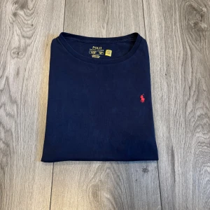 Marinblå t-shirt från Polo Ralph Lauren - Pris går alltid att diskutera, skicka gärna ett bud!       Snygg marinblå t-shirt från Polo Ralph Lauren med klassisk röd broderad logga på bröstet. T-shirten har rund halsringning och är kortärmad, tillverkad i mjuk bomull som känns skön mot huden. Perfekt för en clean och stilren look.