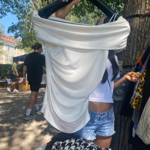 Vit axelbandslös tubtopp - Snygg vit tubtopp med draperad design och offshoulder-look. Toppen är axelbandslös och har en cool, lite oversized passform med snygga rynkade detaljer på sidorna. Perfekt för att skapa en trendig och stilren outfit.