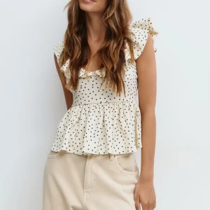 Prickig volangtopp från Gina Tricot - Supersöt topp i beige med svarta prickar från Gina Tricot. Volangdetaljer vid axlar och urringning, öppen rygg med knyt och lätt rynkad midja. Aldrig använd, superfin❤️