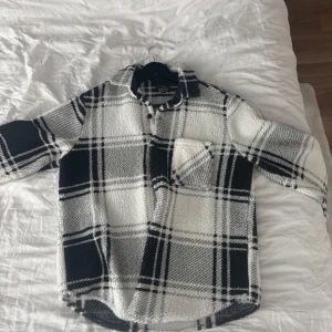 Rutig fleece overshirt från BoohooMAN - Säljer en oversized rutig overshirt från BoohooMAN i svart och vitt fleece-material. Skjortan har klassisk krage, bröstficka och knappar framtill. Perfekt för lager-på-lager och chill stil.