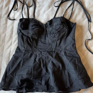 Svart topp med tunna axelband - Säljer en svart topp med tunna axelband och lätt utsvängd nederdel med smockad detalj i ryggen för komfort💞