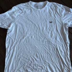 Vit t-shirt från Lee i bomull - Aldrig använd. Klassisk vit t-shirt från Lee med liten broderad logga på bröstet. T-shirten har rund halsringning och korta ärmar. Tillverkad i mjuk bomull och har en normal passform som funkar till det mesta.