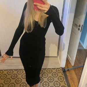 Svart långärmad ribbad klänning - Snygg svart långklänning med lång ärm och fyrkantig ringning. Klänningen är ribbad och har en tight passform som framhäver figuren. Perfekt för dig som gillar en stilren och enkel look med edge.