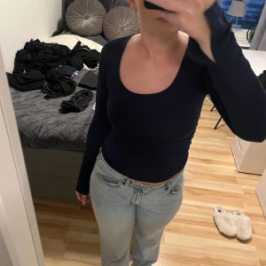 Mörkblå långärmad topp med slits - Säljer en mörkblå långärmad topp med tight passform och rundad, djup urringning. Ärmarna har en cool slitsdetalj vid handleden. Perfekt till jeans för en clean och stilren look. Materialet känns mjukt och stretchigt, troligen bomull eller polyester.