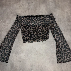 Leopardmönstrad offshoulder topp SHEIN - Trendig croppad offshoulder topp från SHEIN med leopardmönster i svart och beige. Toppens material är tunn och stretchig polyesterblandning, och ärmarna är långa och utsvängda för en extra cool vibe.