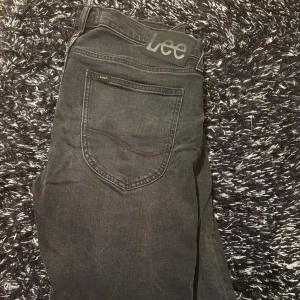 Svarta jeans från Lee - Säljer ett par svarta jeans från Lee med klassisk femficksdesign och Lee-logga på bakfickan. Jeansen har dragkedja och knapp framtill och är tillverkade i mjukt denimtyg. Perfekta för dig som gillar en stilren look.