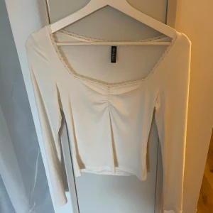 Vit långärmad topp med spetskant - Säljer en söt vit långärmad topp från h&m med spetskant runt den fyrkantiga ringningen och lätt rynk framtill. Toppen är i mjuk ribbad bomull och har en feminin och enkel stil som passar perfekt till jeans eller kjol.